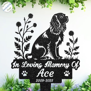 Könnte beinhalten: Schwarzer Metall-Gartenstecker mit Silhouette eines Cavalier King Charles Spaniels, floralen Akzenten und dem Text "In Loving Memory Of Ace 2009-2025". Mit Pfotenabdrücken. Ideal zur Erinnerung an ein geliebtes Haustier.