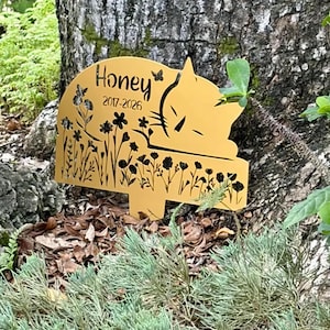 May include: A gold-colored metal garden stake featuring a cutout design of a sleeping cat, wildflowers, and butterflies. The text "Honey" and "2017-2026" are engraved on the surface. The stake has a pointed base for insertion into the ground.