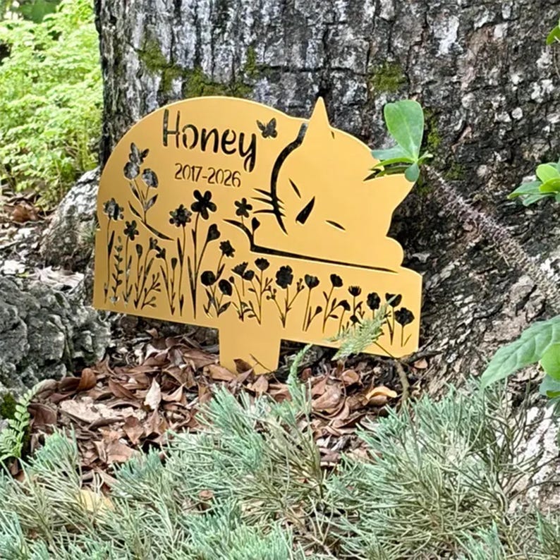 May include: A gold-colored metal garden stake featuring a cutout design of a sleeping cat, wildflowers, and butterflies. The text "Honey" and "2017-2026" are engraved on the surface. The stake has a pointed base for insertion into the ground.
