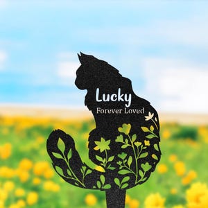 May include: A black metal garden stake shaped like a sitting cat with a cutout floral design. The text "Lucky" and "Forever Loved" is printed in white on the cat's body. The design features intricate leaf and flower patterns throughout.