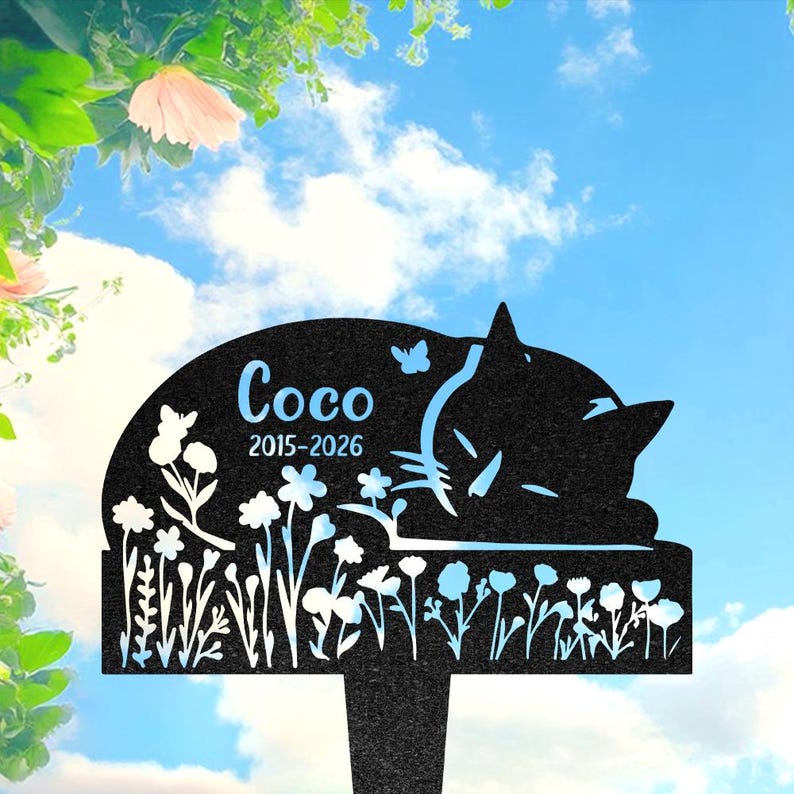 May include: A black metal garden stake featuring a silhouette of a sleeping cat surrounded by flowers and butterflies. The text Coco and the years 2015-2026 are engraved on the surface. The design includes a pointed base for insertion into soil.