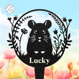 May include: Black metal garden stake featuring a stylized rat design with the word "Lucky" at the base. The rat is surrounded by floral and plant elements within a circular frame. The background is a blurred image of flowers and sky.