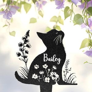 May include: A black silhouette of a sitting cat featuring the name Bailey in white script lettering. The cat design includes cut-out details of various flowers, leaves, and small paw prints integrated into its body, mounted on a thin stake.