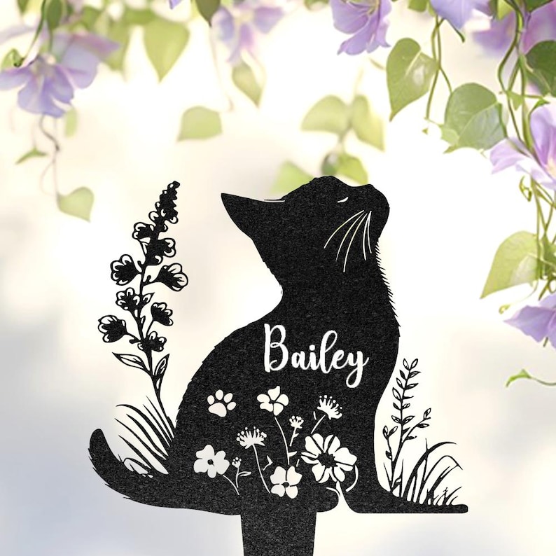 May include: A black silhouette of a sitting cat featuring the name Bailey in white script lettering. The cat design includes cut-out details of various flowers, leaves, and small paw prints integrated into its body, mounted on a thin stake.