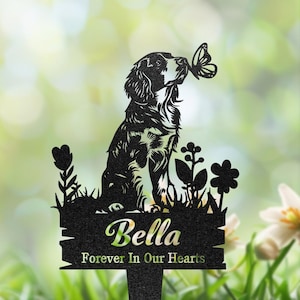 Könnte beinhalten: Schwarzer Metall-Gartenstecker mit einer Hundesilhouette und einem Schmetterling. Der Stecker trägt den Namen "Bella" und den Satz "Forever In Our Hearts" in einer dekorativen Schriftart, mit floralen Details.
