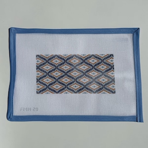 May include: A rectangular needlepoint canvas with a geometric diamond pattern in shades of navy blue, light blue, and brown. The canvas is surrounded by a light blue border.