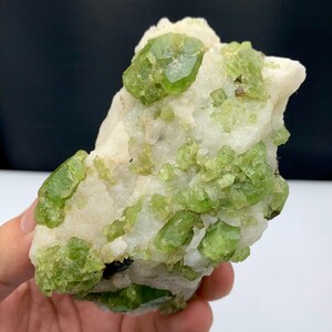 Puede incluir: Primer plano de un espécimen mineral con cristales verdes brillantes incrustados en una matriz blanca. Los cristales varían en tamaño y forma, algunos con estructuras facetadas bien definidas. La textura general es áspera y desigual.