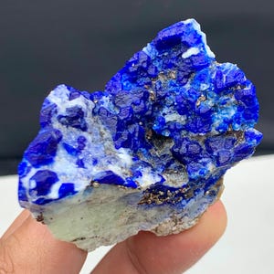 Puede incluir: Un vibrante espécimen de lapislázuli en bruto. El mineral azul profundo está salpicado de pirita dorada y calcita blanca, creando un contraste llamativo. La piedra tiene una textura rugosa y natural y una base verde claro.