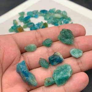Puede incluir: Una colección de piedras preciosas en bruto, sin cortar, en tonos turquesa y verde azulado. Las piedras varían en tamaño y forma, con una textura rugosa y natural. Algunas piedras son de un azul verdoso intenso y saturado, otras más claras.