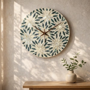 May include: A circular wall clock featuring a mosaic pattern of dark teal and cream-coloured petal shapes. The clock face has a smooth, reflective surface with three thin, dark brown metal hands positioned at the centre to indicate the time.