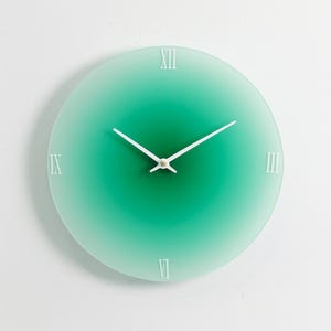 May include: A circular wall clock with a green gradient face. White Roman numerals and white hands display the time. The clock has a modern, minimalist design, suitable for any room.