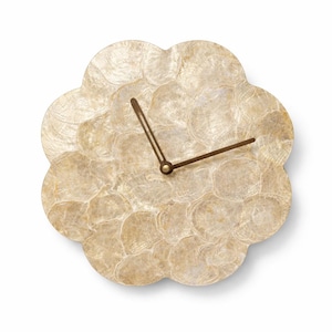 Puede incluir: Un reloj de pared con forma de flor y acabado de nácar. La esfera del reloj está compuesta por piezas de concha iridiscentes superpuestas en tonos crema y beige. Las manecillas del reloj son de color bronce oscuro.