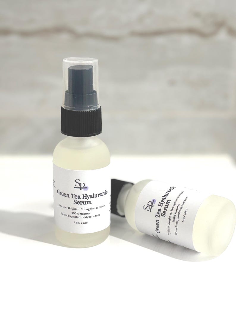 May include: Two clear glass spray bottles of Green Tea Hyaluronic Serum. The bottles have white labels with black text and a logo. The serum is a light green colour. The bottles are 30ml.