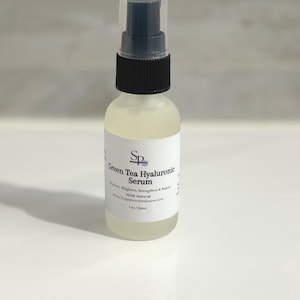 May include: A clear glass bottle of Green Tea Hyaluronic Serum with a black and clear spray top. The label reads "Green Tea Hyaluronic Serum" and "Hydrate, Brighten, Strengthen & Repair". The bottle contains 30ml of serum.