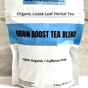 May include: A white pouch with a blue band, labeled "SUGA PLUM BODYCARE LLC" and "Organic Loose Leaf Herbal Tea." The text "BRAIN BOOST TEA BLEND" is prominent. It states "100% Organic / Caffeine Free." The pouch contains 2.5oz, 30 servings.