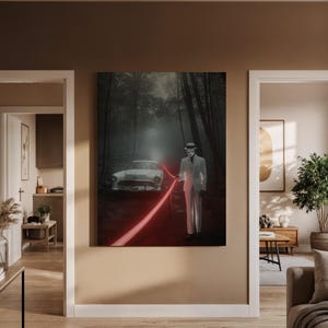 May include: A framed canvas art print depicts a surreal scene. A figure in a white suit and hat stands in a dark forest, holding a glowing red line that leads to a vintage white car. The artwork has a mysterious, cinematic quality.