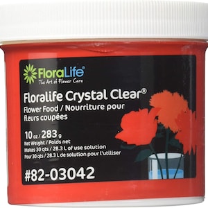 May include: A red plastic container of Floralife Crystal Clear flower food. The label includes the Floralife logo, product name, and details about the net weight (10 oz / 283 g) and solution yield. The container has a white lid and features a floral illustration.