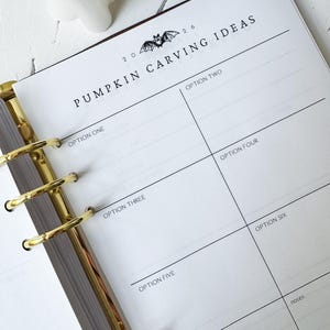 May include: A white planner page with gold metal rings featuring the text 2026 PUMPKIN CARVING IDEAS with a bat illustration. The page is divided into six sections labeled OPTION ONE through OPTION SIX, plus a section for notes and FINAL CHOICE.