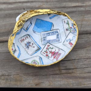 May include: A decorative oyster shell dish with a gold-painted rim. The interior features a decoupage pattern of various playing cards and mahjong tiles, including a card labeled JOKER, against a white background with blue and red accents.