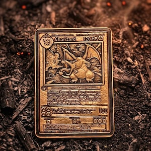 Può includere: Una carta rettangolare in metallo color oro con un design in rilievo del personaggio Charizard. La carta mostra il nome Charizard, 120 HP e un testo dettagliato che include Flame Pokémon, Energy Burn e Fire Spin con 100 danni.