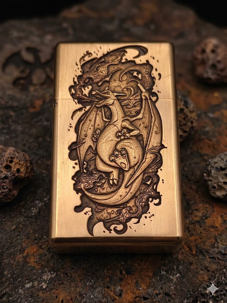 May include: A brass-colored lighter with a detailed dragon engraving. The dragon is depicted with wings and is surrounded by swirling smoke or clouds. The lighter has a rectangular shape and a hinged lid.