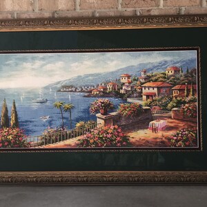 May include: Framed landscape art print depicting a coastal town with red-roofed buildings, palm trees, and sailboats on the water. The artwork is framed in a gold-toned, ornate frame with a dark green matting.