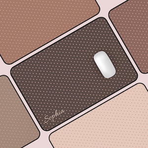 May include: A computer mouse on a brown mousepad with a polka dot pattern. The mousepad is surrounded by other brown and tan polka dot squares. The name "Sophia" is written in cursive on the mousepad.