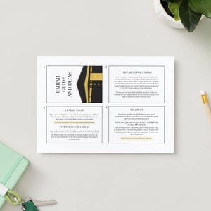 Puede incluir: Una guía impresa en blanco titulada "Umrah Guide and Du'as" con un gráfico dorado y negro. La guía está sobre una superficie blanca con un cuaderno verde, un lápiz y una pequeña planta en el fondo.