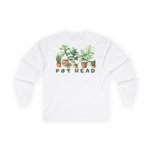 Könnte beinhalten: Weißes Langarmshirt mit einer Aquarellillustration verschiedener Topfpflanzen. Der grüne Text "POT HEAD" ist unter den Pflanzen aufgedruckt. Das Shirt besteht aus einem weichen, bequemen Material.