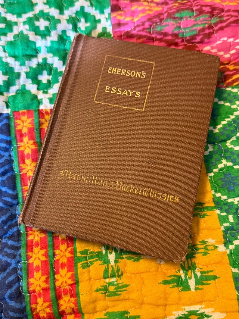 May include: A brown hardcover book titled "Emerson's Essays" from Macmillan's Pocket Classics. The book is set against a colorful patchwork quilt background with green, yellow, pink, and blue patterns. The book's cover has gold lettering.