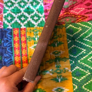 May include: A brown book spine with visible wear and tear. The book's cover is a dark brown color, and the spine shows signs of age. The background is a colorful patchwork quilt with various patterns and colors.