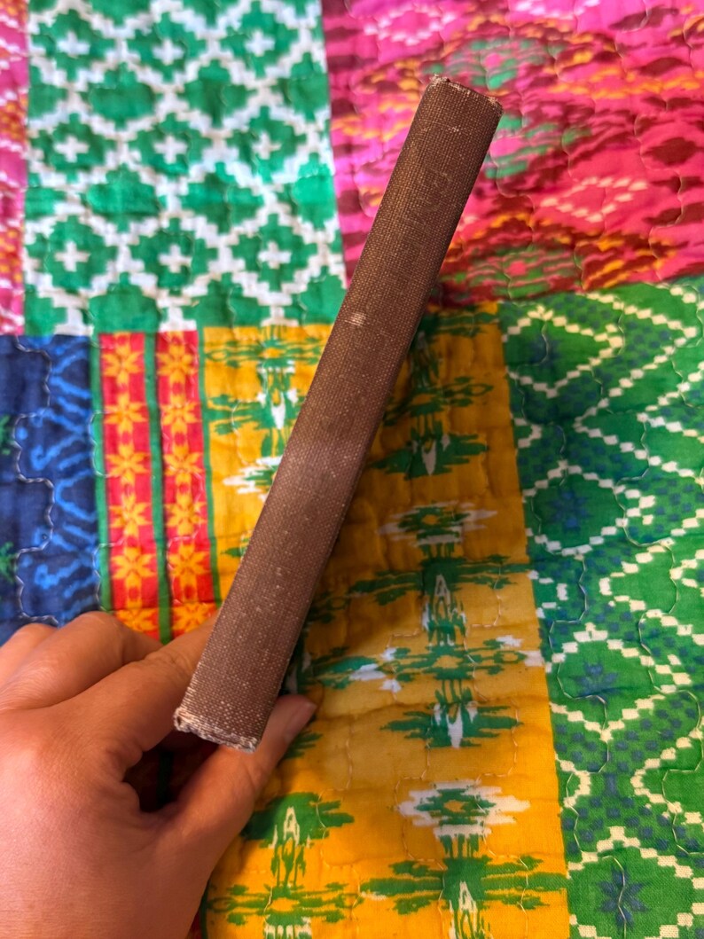 May include: A brown book spine with visible wear and tear. The book's cover is a dark brown color, and the spine shows signs of age. The background is a colorful patchwork quilt with various patterns and colors.
