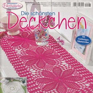 以下が含まれることがあります： 「Die schönsten Deckchen」というタイトルと「Dekorative Blickfänge für Ihr Zuhause」というテキストが書かれた、ピンクのクロシェのテーブルランナーが載っている雑誌の表紙です。