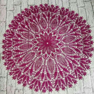 May include: A large, round, crocheted doily in a deep magenta color. The doily has a delicate, intricate design with a central flower motif.