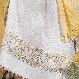 May include: A white linen towel with a decorative crocheted border. The towel has horizontal stitched lines and a scalloped edge. A yellow and white striped towel with tassels is also visible.