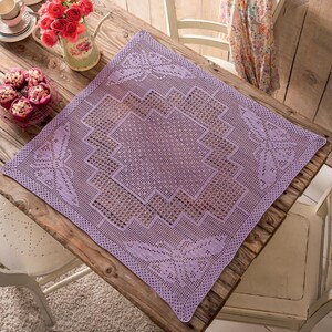 Pode incluir: Uma toalha de mesa quadrada de crochê na cor lavanda com um design detalhado em renda. A toalha de mesa apresenta um padrão geométrico central e motivos florais decorativos em cada canto. A textura intrincada, semelhante à renda, adiciona um toque delicado ao têxtil.