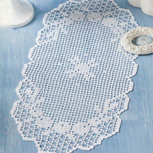 Pode incluir: Doily oval de crochê branco com um delicado padrão de renda. O doily é feito com um fio fino e tem uma borda festonada.