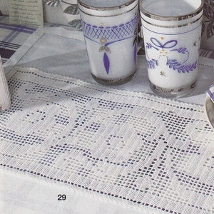 May include: White crocheted table runner with a delicate pattern. The runner has a blue and white design and is placed on a white tablecloth. The runner is 29 inches long.