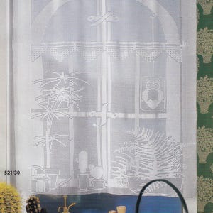 May include: White crocheted window curtain with a detailed design. The curtain features an arched top and a pattern depicting a window scene with plants. The number "521/30" is visible in the lower left corner. The curtain is hanging in front of a window.