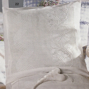 Può includere: Un cuscino bianco all'uncinetto con un delicato motivo floreale. Il cuscino è seduto su una sedia bianca con un cuscino a quadri bianchi e blu dietro. Il numero 22 è visibile nell'angolo in alto a sinistra dell'immagine.