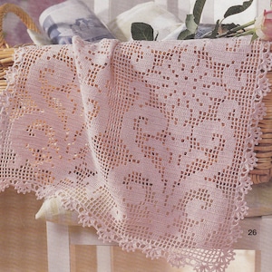 Op de afbeelding: Een delicate roze gehaakte doily met een bloemenpatroon, gedrapeerd over een rieten mand en een witte stoel.