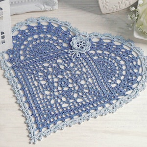 May include: A blue and white crocheted heart-shaped doily with a small crocheted flower in the center.