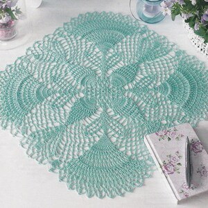 May include: A light blue crocheted doily with a delicate, intricate design. The doily is laid flat on a white surface.