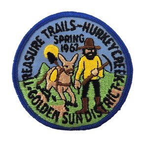 May include: A blue and yellow embroidered patch with the text "Treasure Trails - Hunkey Creek - Golden Sundials Spring 1967". The patch features a cartoon image of a person with a beard and a donkey.