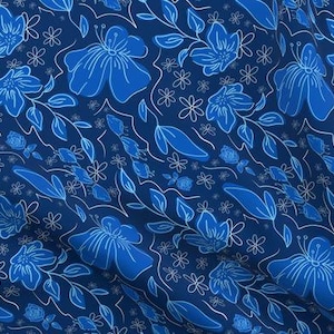 May include: A fabric with a repeating floral pattern in shades of blue and white. Large, stylized blue flowers and leaves are outlined in white against a dark blue background. Smaller white flowers and vines complete the design.