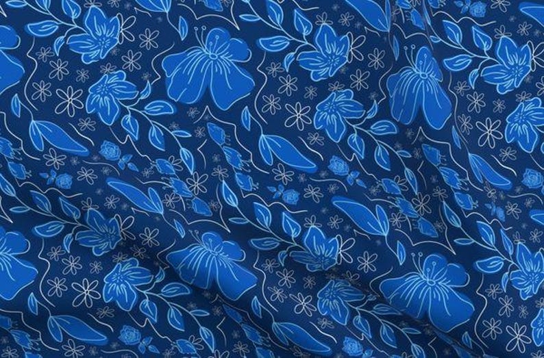May include: A fabric with a repeating floral pattern in shades of blue and white. Large, stylized blue flowers and leaves are outlined in white against a dark blue background. Smaller white flowers and vines complete the design.
