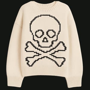 May include: Cream-colored sweater featuring a pixelated black skull and crossbones design. The crew neck sweater has long sleeves and ribbed cuffs and hem. A casual, gothic-inspired garment.