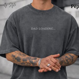 May include: Dark gray, oversized t-shirt with the text "DAD LOADING..." in white. The shirt has a crew neck and short sleeves. The word "Pepper" is in the upper right corner. The brand name "Diagonally Style" is in the upper left corner.