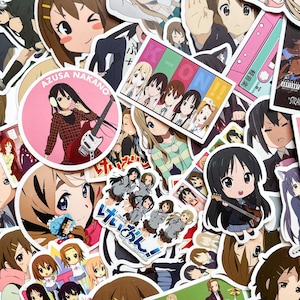 Pode incluir: Uma cole&ccedil;&atilde;o de autocolantes em estilo anime com v&aacute;rios personagens. Os autocolantes mostram uma variedade de poses e express&otilde;es, alguns segurando instrumentos musicais. A paleta de cores inclui rosa, azul, castanho e branco.