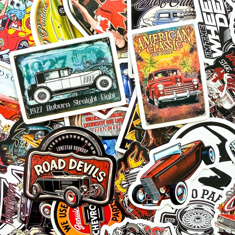 May include: A collection of vintage car-themed stickers. Featured are stickers with classic car illustrations, including a 1927 Auburn Straight Eight, a 1947 Ford, and a Road Devils design. The stickers have a retro aesthetic.